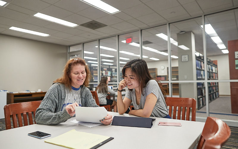 Two females looking at a tablet and paper working on a class schedule