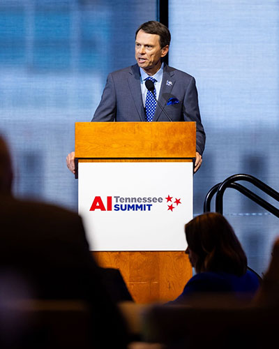 University of Memphis President Bill Hardgrave speaking at a podium during the AI Tennessee Summit in Nashville.
