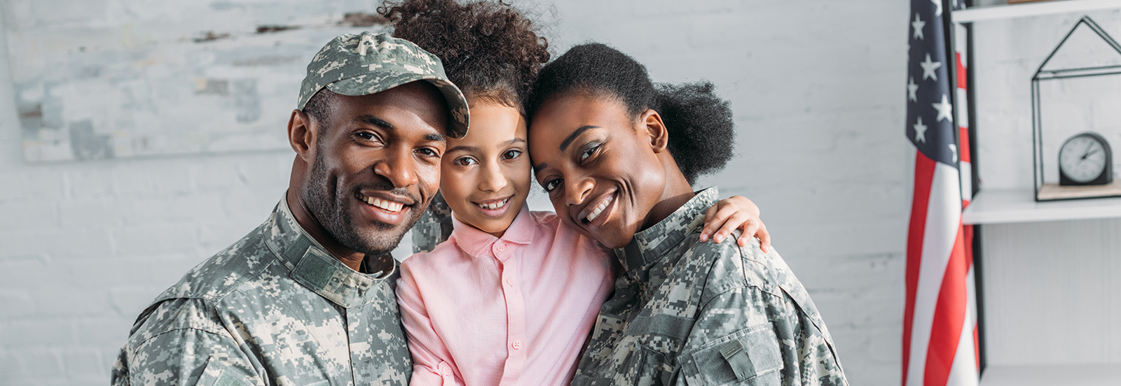 Military family (father, daughter, and mom) smiling with an American flag in the background