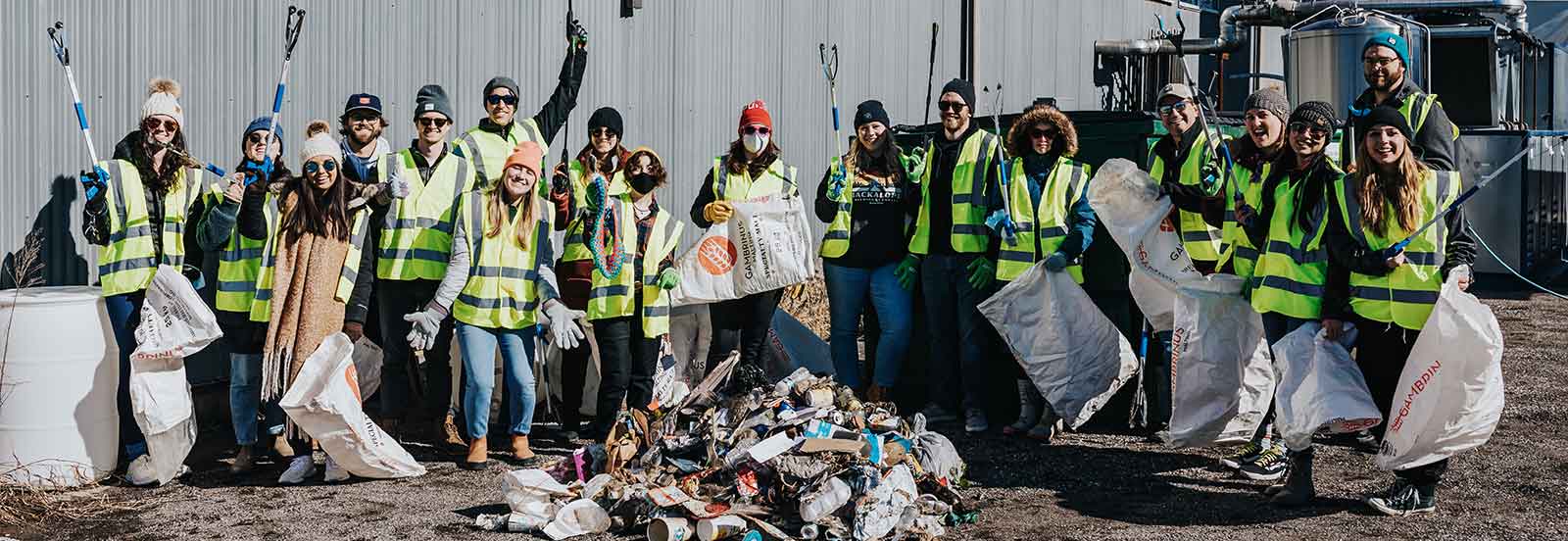 A group of volunteers at a Keep TN Beautiful cleanup event stand with reusable litter bags and litter pickers in front of a pile of trash at a litter cleanup.