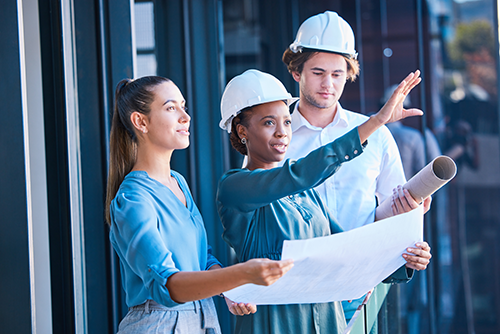 three people on construction site holding blueprints