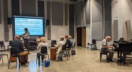 Music theraphy class lead by professor on guitar surrounded by a group of senior adults