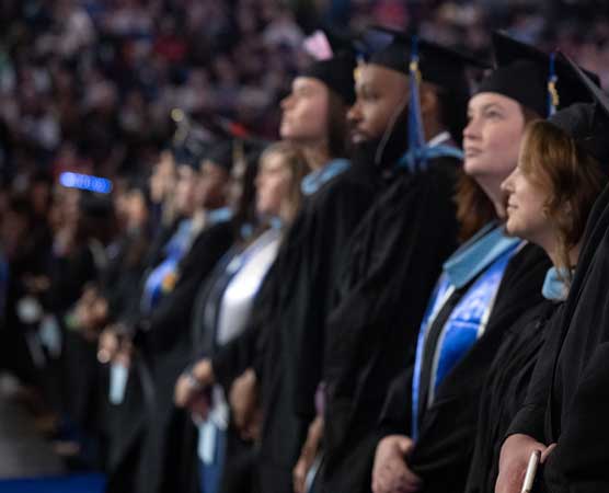 UofM students standing at commencement ceremony in cap and gown