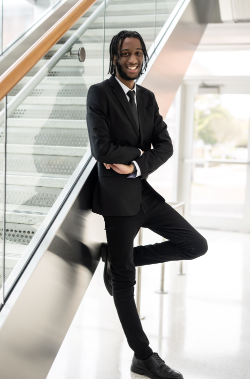 Student in Suit leaning against a staircase